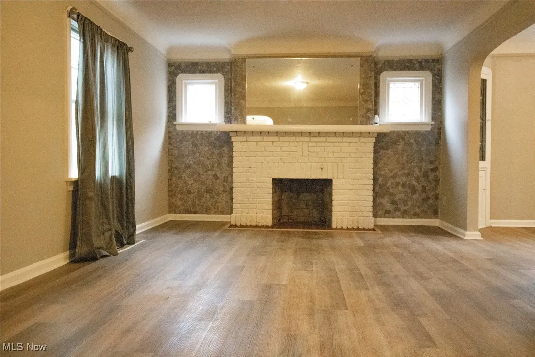 Unfurnished living room featuring baseboards, arched walkways, wood finished floors, and a brick fireplace