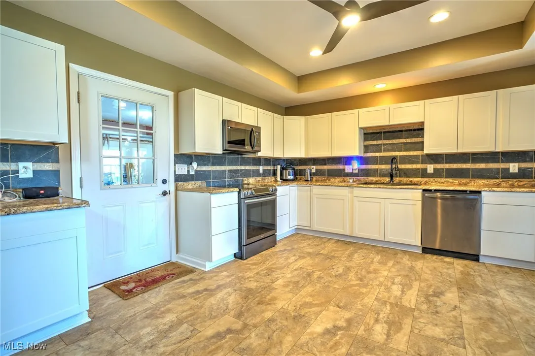 Kitchen with ceiling fan, stainless steel appliances, a sink, a tray ceiling, and backsplash