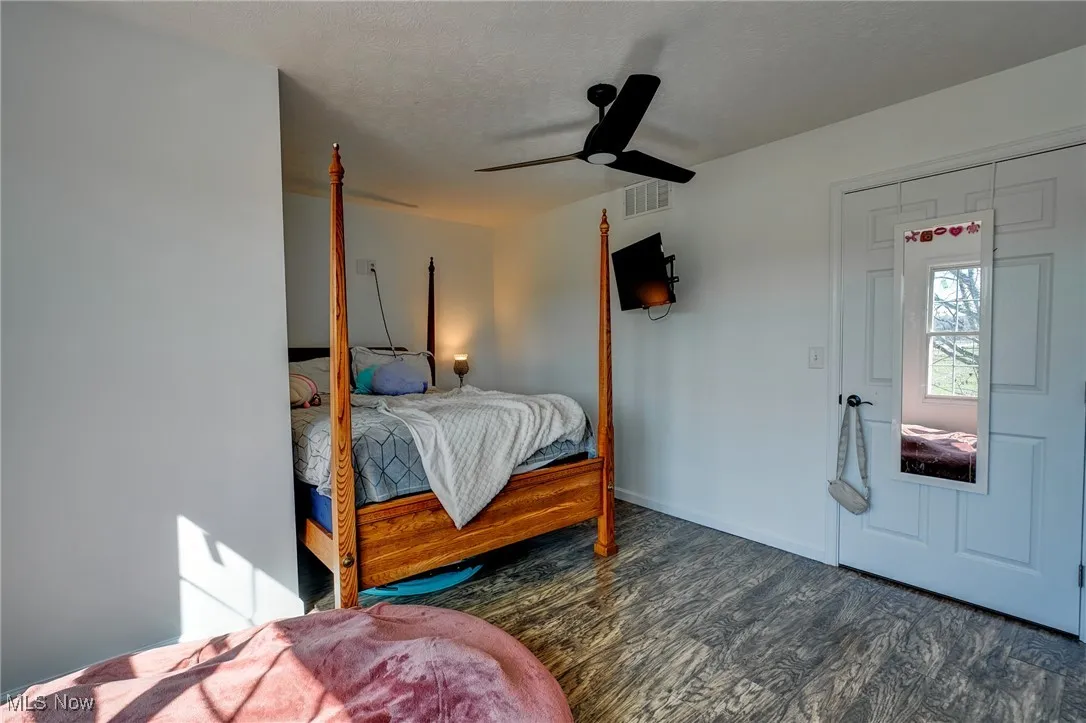 Bedroom with a ceiling fan, wood finished floors, a textured ceiling, baseboards, and visible vents