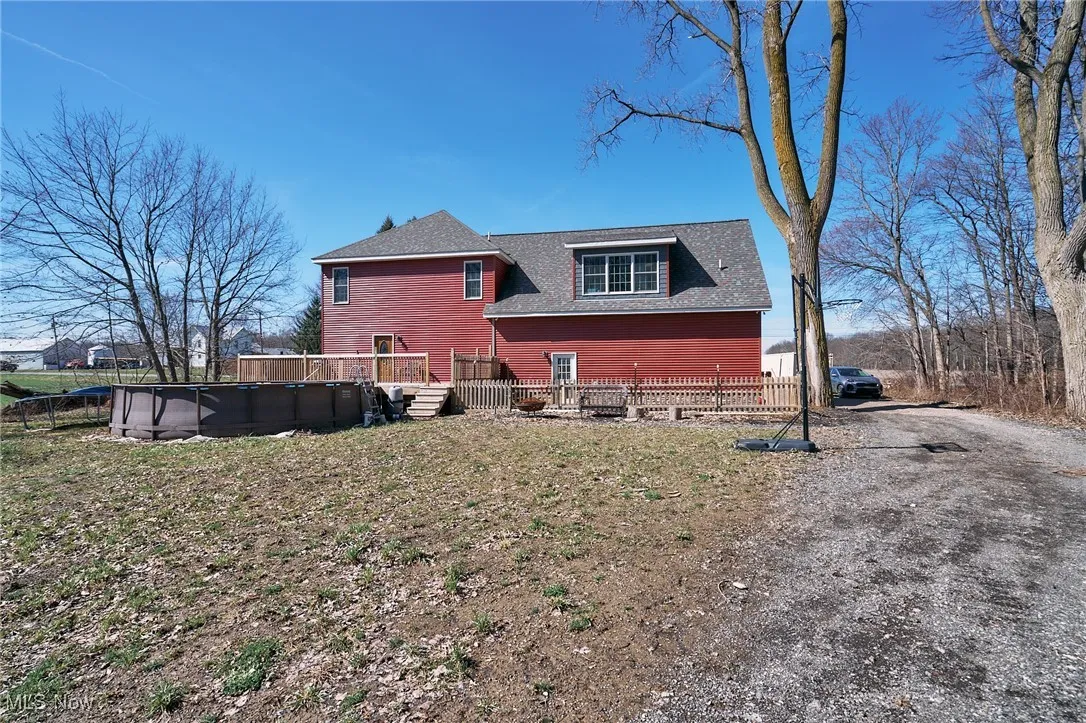 Rear view of property with roof with shingles, fence, a wooden deck, driveway, and a fenced in pool