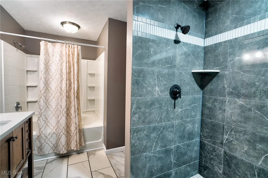 Bathroom with marble finish floor, vanity, shower / tub combo, and a textured ceiling