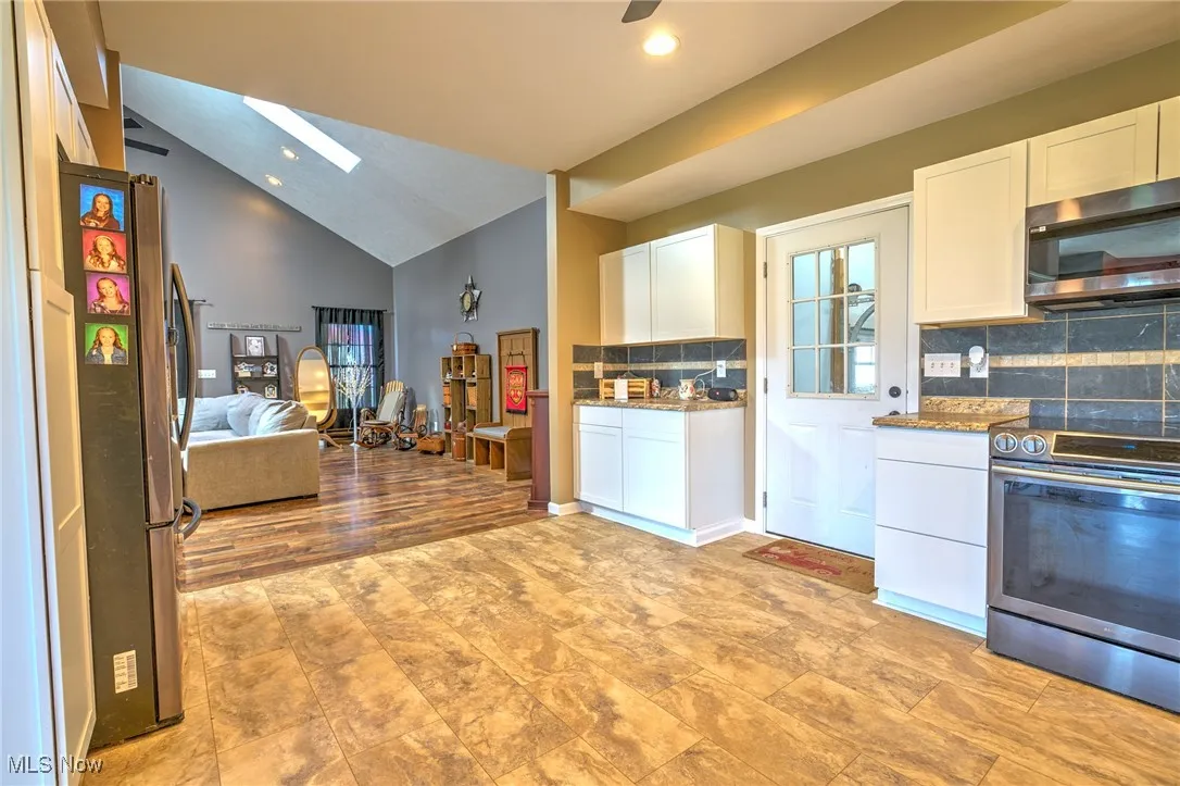 Kitchen with open floor plan, white cabinets, light stone countertops, and stainless steel appliances