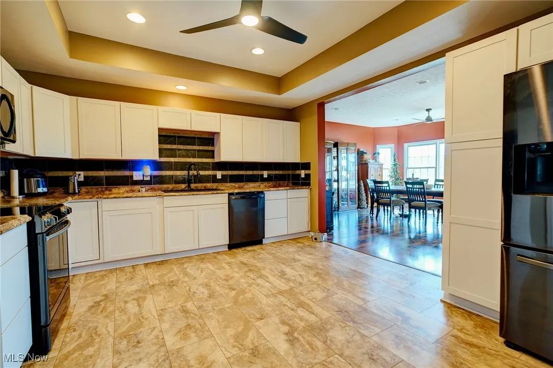 Kitchen featuring a raised ceiling, a sink, black appliances, and ceiling fan