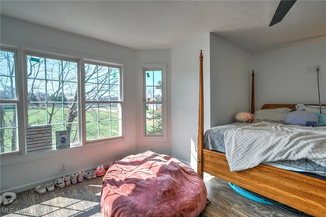 Bedroom featuring a textured ceiling, ceiling fan, wood finished floors, and multiple windows