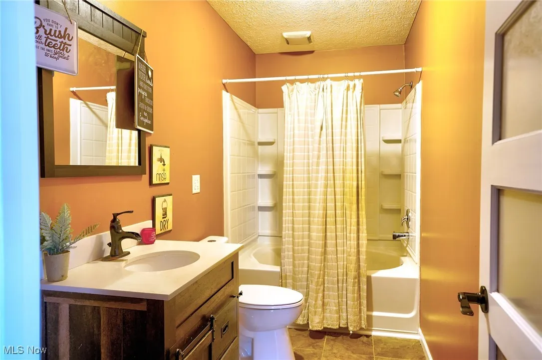 Full bath with tile patterned flooring, vanity, toilet, a textured ceiling, and shower / bath combo