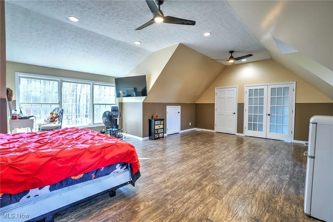 Bedroom with a textured ceiling, lofted ceiling, wood finished floors, and freestanding refrigerator