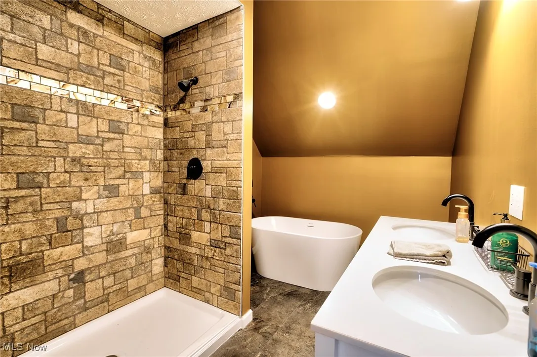 Full bath with lofted ceiling, a sink, and a stall shower