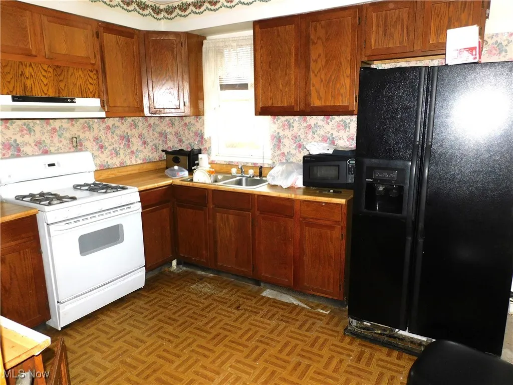 Kitchen with light countertops, under cabinet range hood, wallpapered walls, a sink, and black appliances