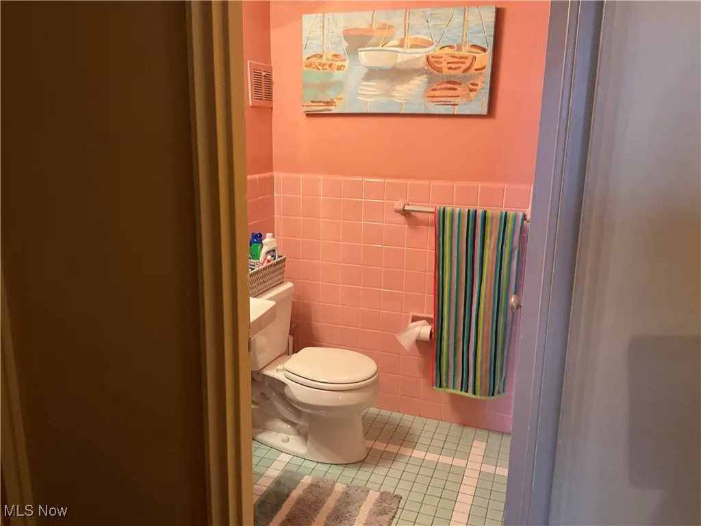 Bathroom featuring tile walls, toilet, tile patterned floors, visible vents, and wainscoting