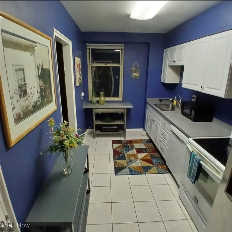 Kitchen with white appliances, light tile patterned flooring, white cabinets, and light countertops