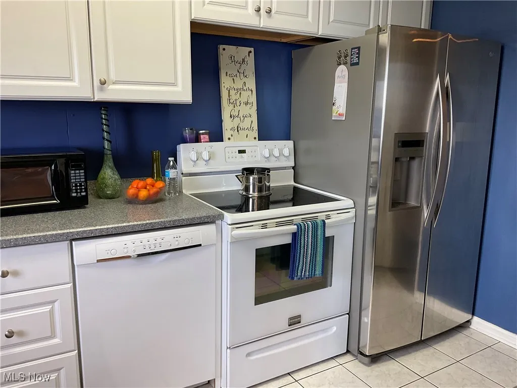 Kitchen with white cabinets, dark countertops, light tile patterned floors, and white appliances