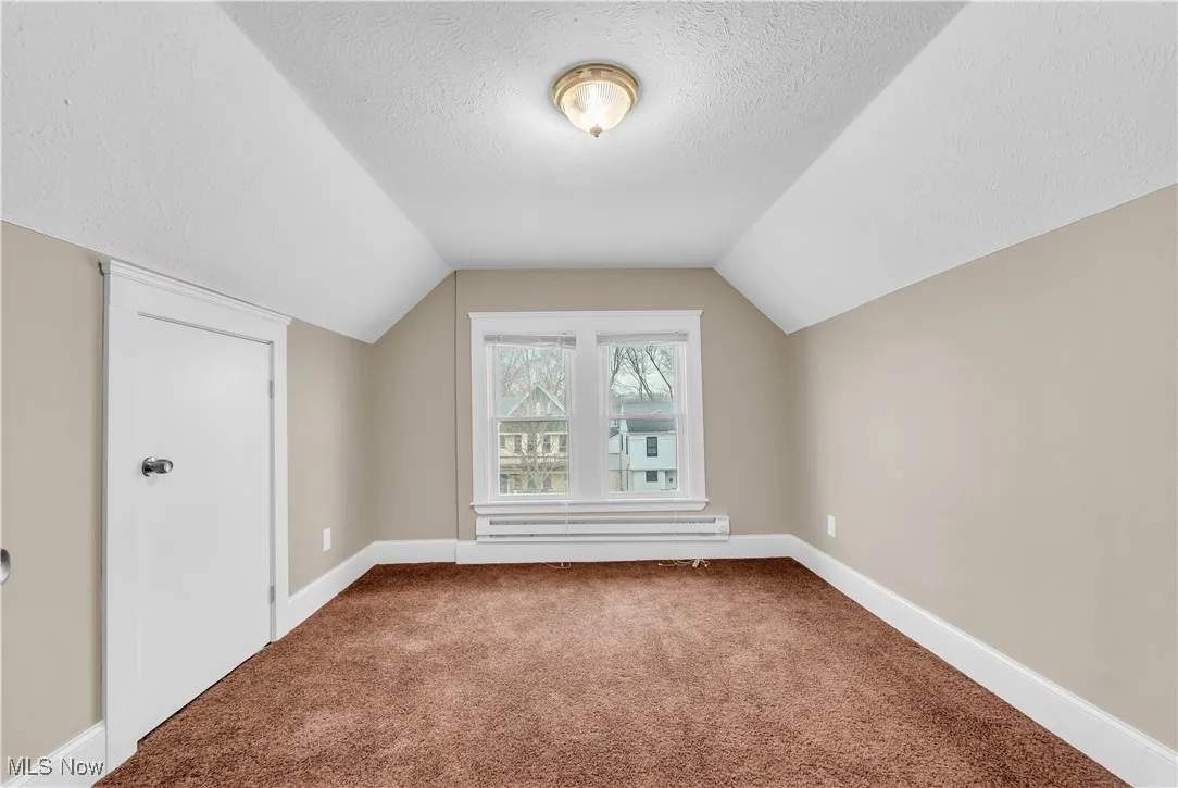 Bonus room featuring lofted ceiling, a baseboard heating unit, carpet flooring, baseboards, and a textured ceiling