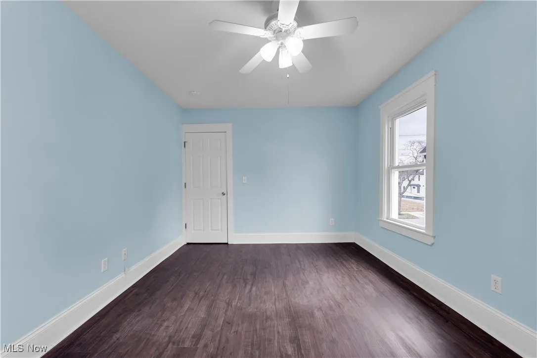 Empty room with dark wood finished floors, baseboards, and a ceiling fan