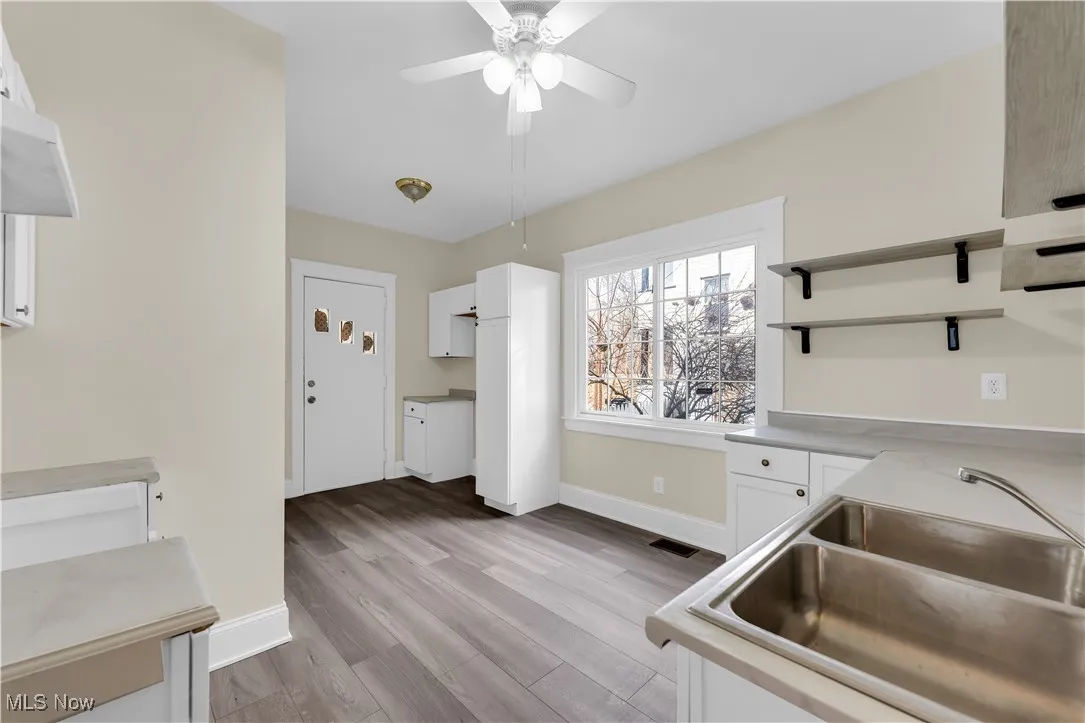 Kitchen featuring white cabinetry, open shelves, light wood-type flooring, a sink, and visible vents