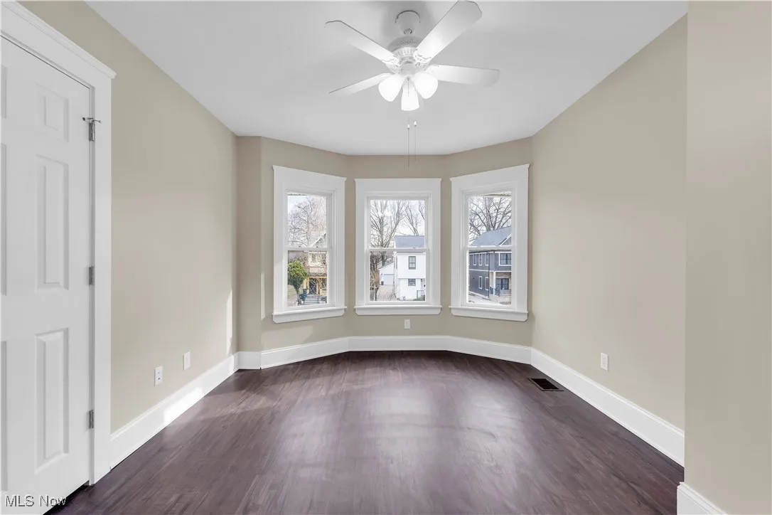 Spare room with baseboards, visible vents, ceiling fan, and dark wood-type flooring