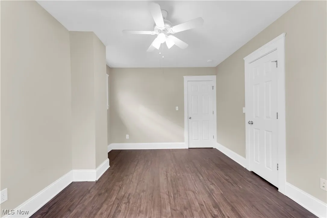 Unfurnished room featuring dark wood-type flooring, baseboards, and ceiling fan