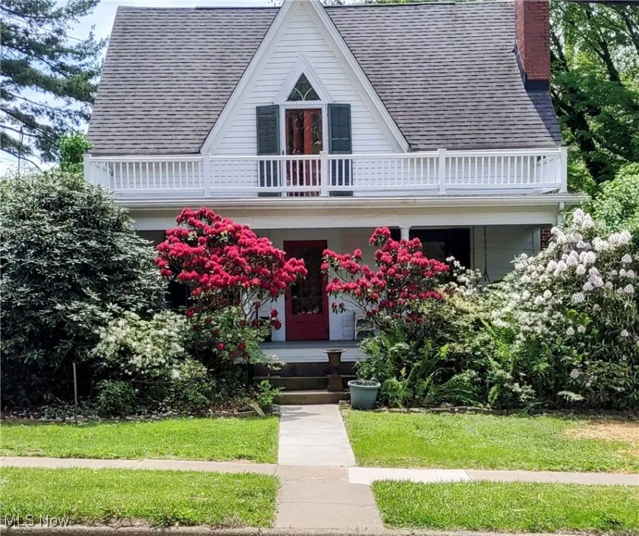 View of front of house featuring a balcony, a chimney, roof with shingles, and a porch