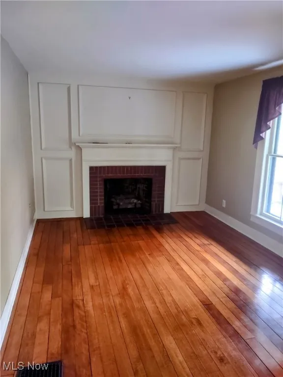 Unfurnished living room with hardwood / wood-style floors, a brick fireplace, baseboards, and visible vents