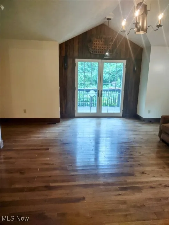 Unfurnished living room featuring wooden walls, baseboards, wood finished floors, vaulted ceiling, and a notable chandelier