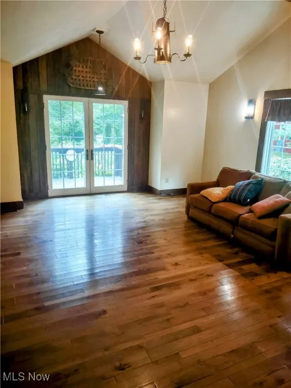 Living room featuring a healthy amount of sunlight, vaulted ceiling, an inviting chandelier, and wood-type flooring