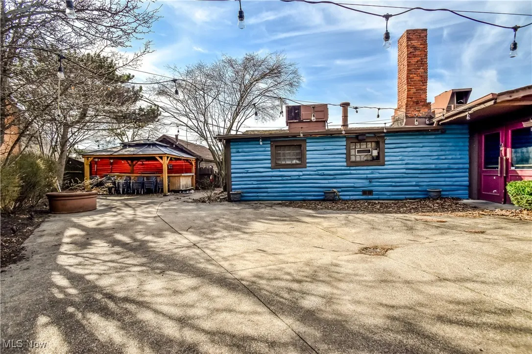 View of property exterior featuring faux log siding, a chimney, a patio, and a gazebo
