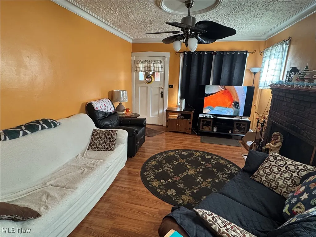Living room with a textured ceiling, wood finished floors, a ceiling fan, and crown molding