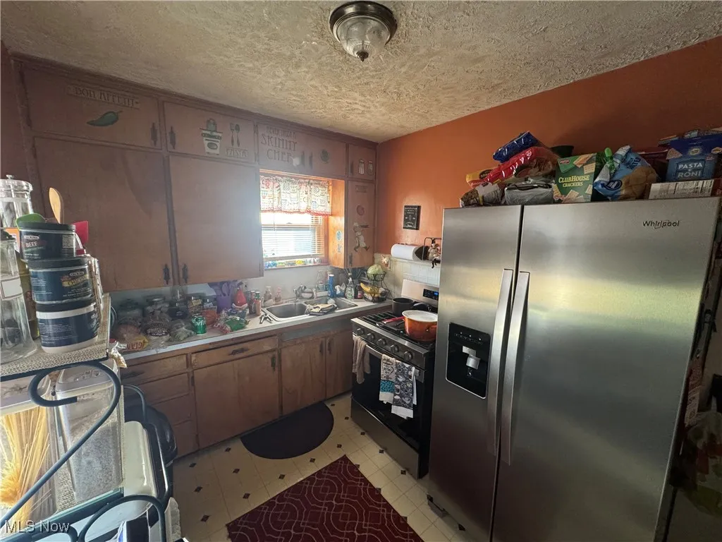 Kitchen with light countertops, a textured ceiling, a sink, appliances with stainless steel finishes, and light floors