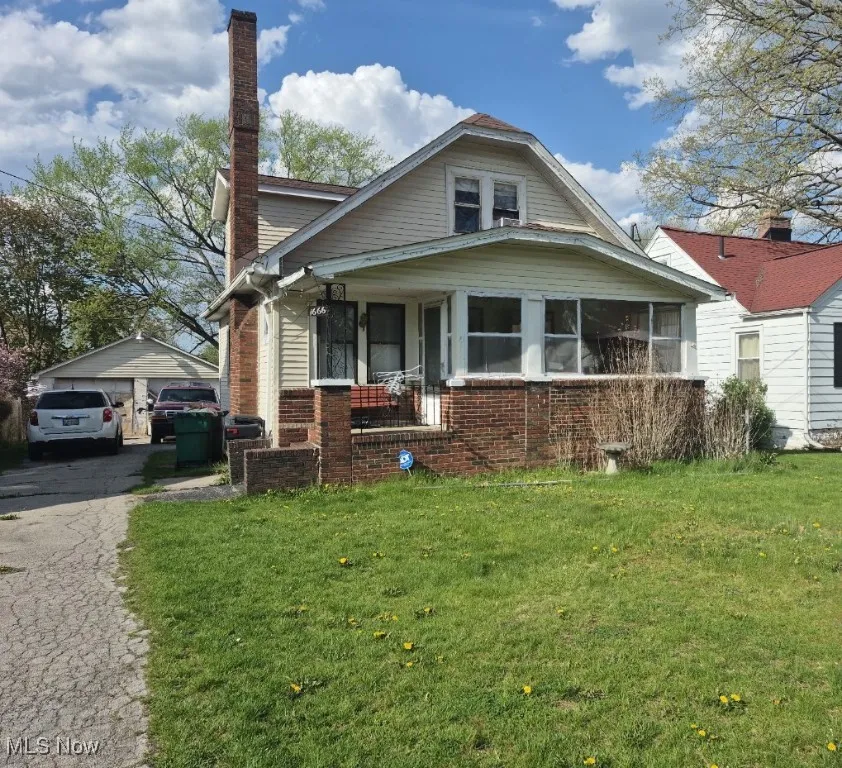Bungalow-style house featuring a front lawn, a chimney, brick siding, and a garage