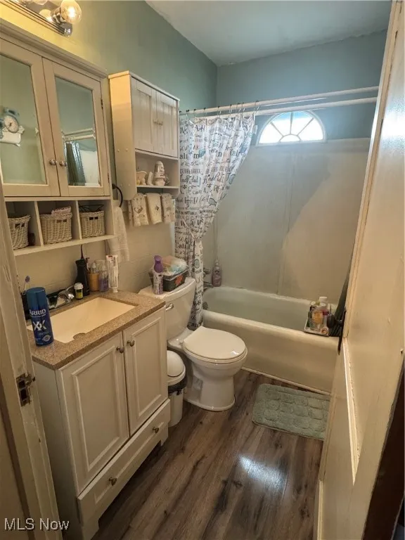 Full bath featuring toilet, vanity, tasteful backsplash, wood finished floors, and shower / bath combo with shower curtain