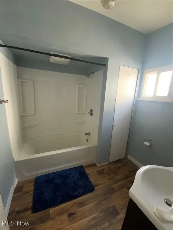 Bathroom featuring  shower combination, baseboards, wood finished floors, and a sink