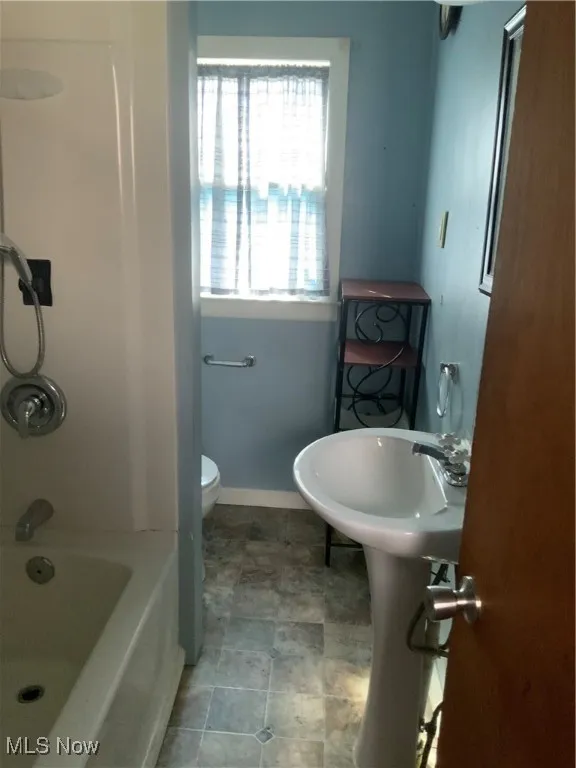 Bathroom featuring baseboards, toilet, and shower / bathtub combination