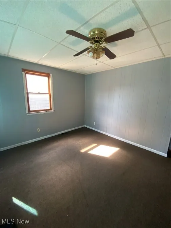 Unfurnished room with a paneled ceiling, baseboards, dark carpet, and ceiling fan
