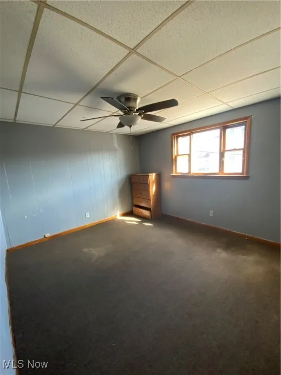 Empty room with carpet flooring, a paneled ceiling, baseboards, and ceiling fan
