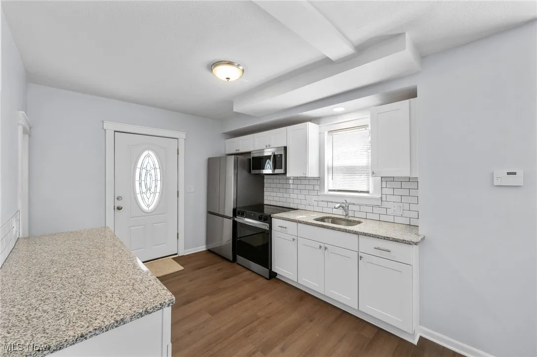 Kitchen with white cabinets, a sink, wood-style flooring, tasteful backsplash, and appliances with stainless steel finishes