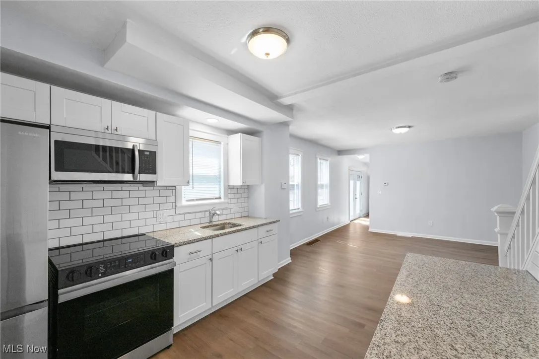 Kitchen featuring a sink, white cabinetry, backsplash, wood style floors, and appliances with stainless steel finishes