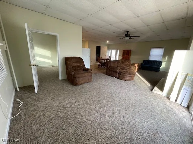Unfurnished living room featuring carpet flooring, ceiling fan, and a drop ceiling