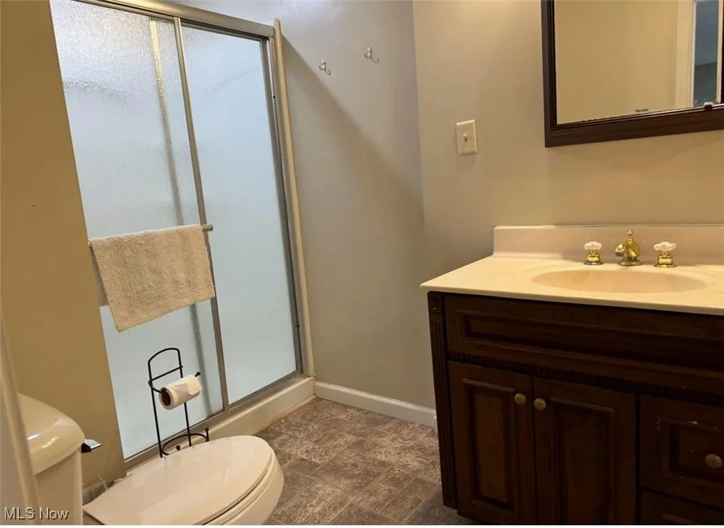 Full bathroom featuring toilet, vanity, baseboards, and a shower stall