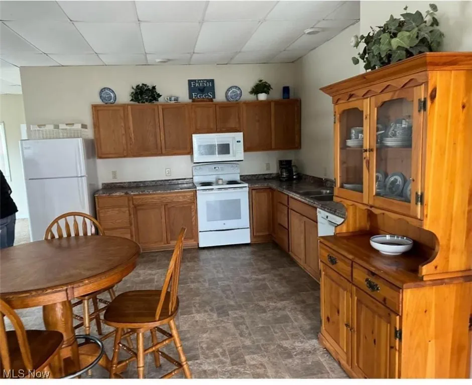 Kitchen with a drop ceiling, countertops, brown cabinetry, and white appliances