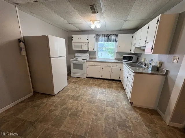 Upstairs Apartment Kitchen with white appliances, a paneled ceiling, white cabinets, and stone finish floors