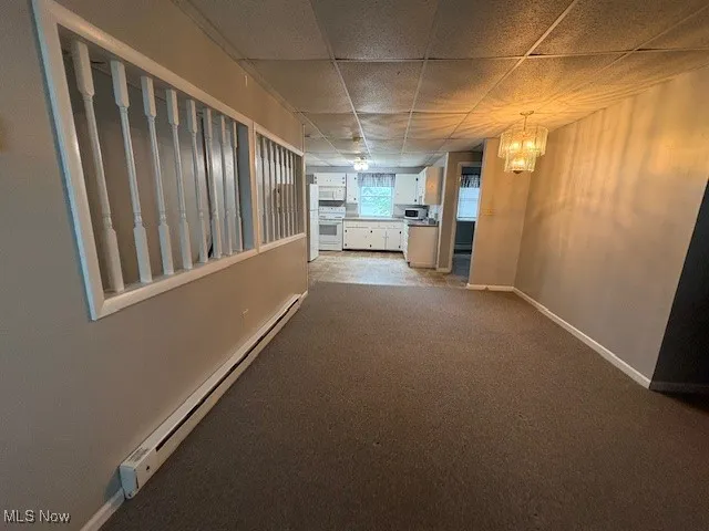 Hallway featuring a baseboard heating unit, a chandelier, a paneled ceiling, and carpet flooring