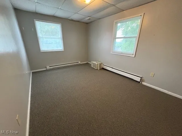 Carpeted empty room featuring baseboard heating, a baseboard heating unit, healthy amount of natural light, and a paneled ceiling