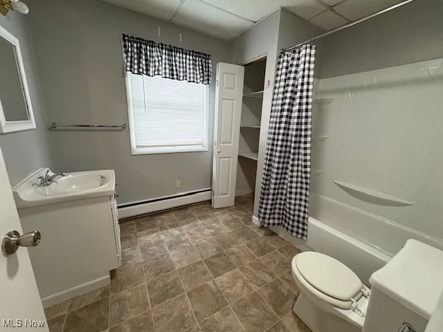 Full bathroom featuring a baseboard heating unit, a drop ceiling, vanity, and shower / tub combo with curtain