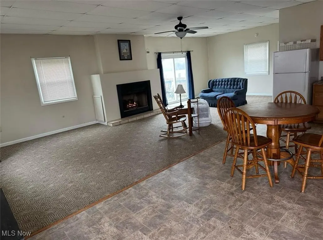 Carpeted dining room featuring a ceiling fan, baseboards, a lit fireplace, and a paneled ceiling
