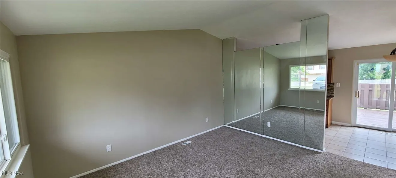 Carpeted empty room with lofted ceiling and baseboards
