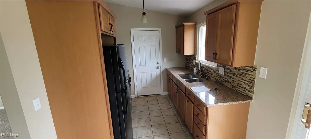 Kitchen featuring freestanding refrigerator, tasteful backsplash, light tile patterned flooring, light stone counters, and brown cabinets