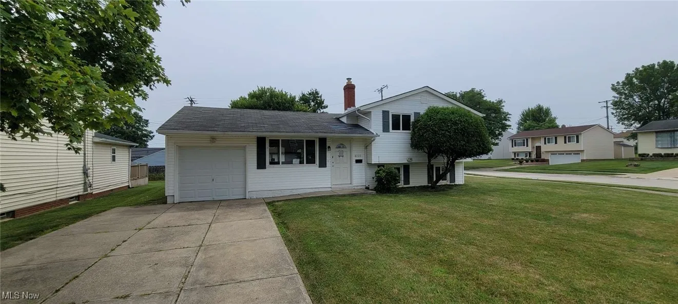 View of front of property with concrete driveway, a front yard, a chimney, and an attached garage
