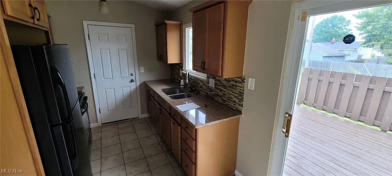 Kitchen with freestanding refrigerator, decorative backsplash, light tile patterned flooring, and brown cabinets