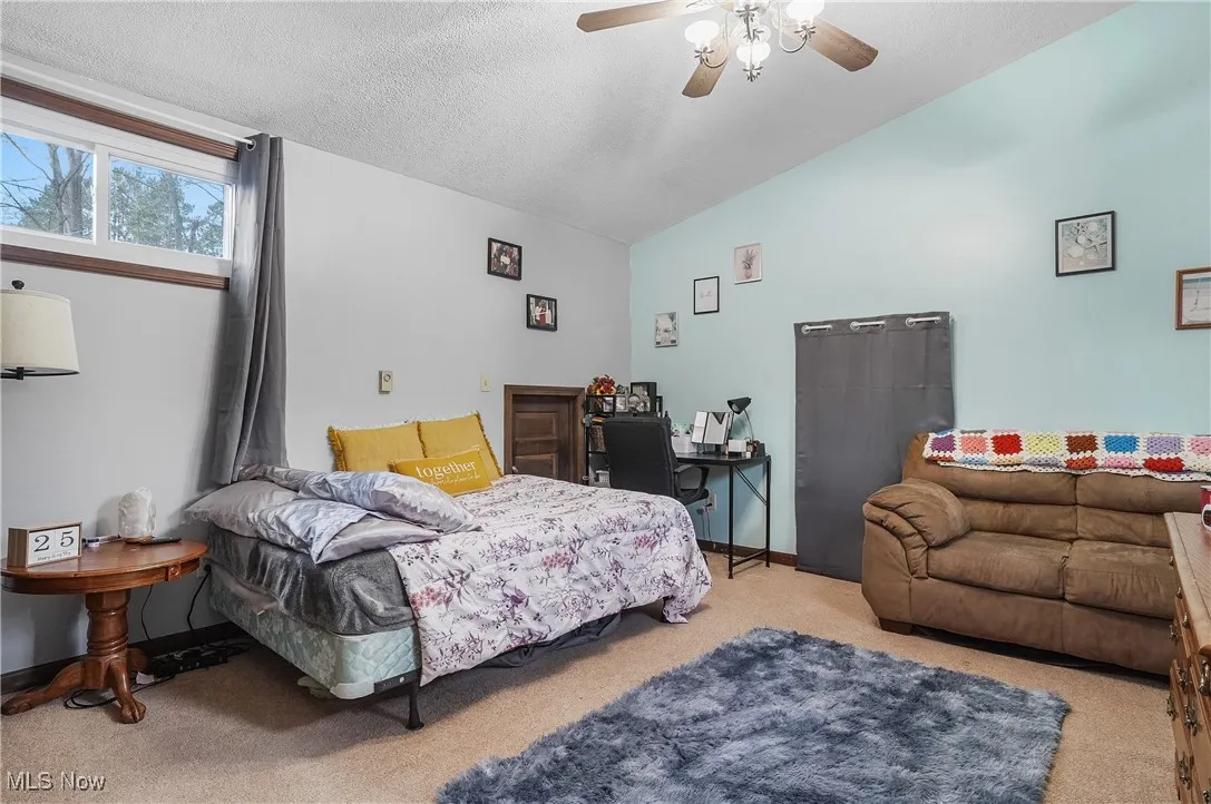 Bedroom with a textured ceiling, lofted ceiling, baseboards, ceiling fan, and carpet