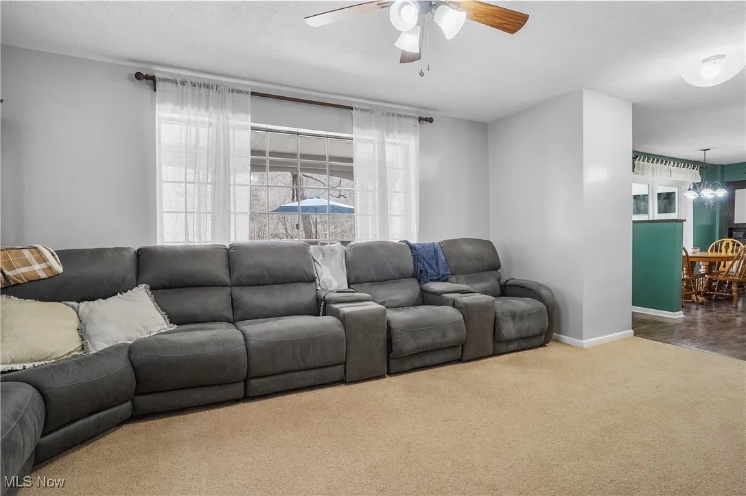 Living area featuring ceiling fan with notable chandelier, baseboards, and carpet flooring