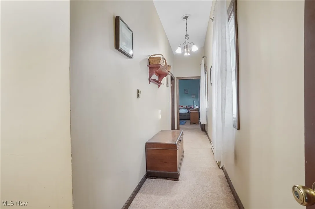 Hallway featuring light carpet, baseboards, and a notable chandelier